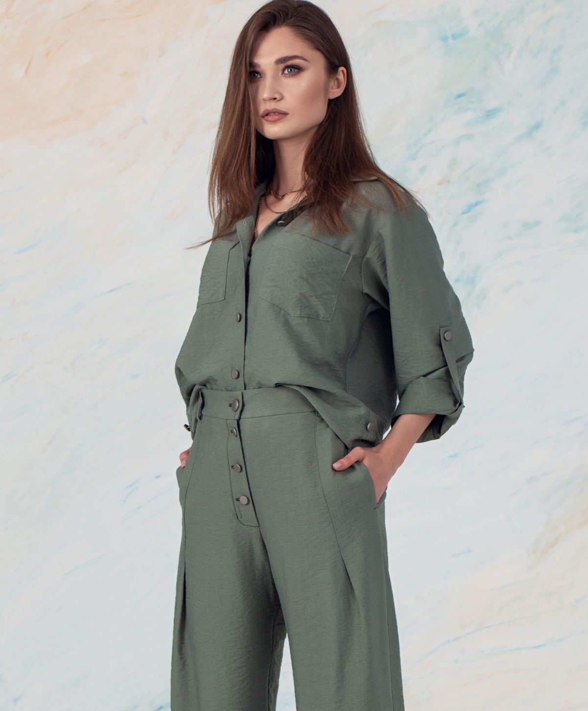 Model wearing stylish green outfit against abstract background.