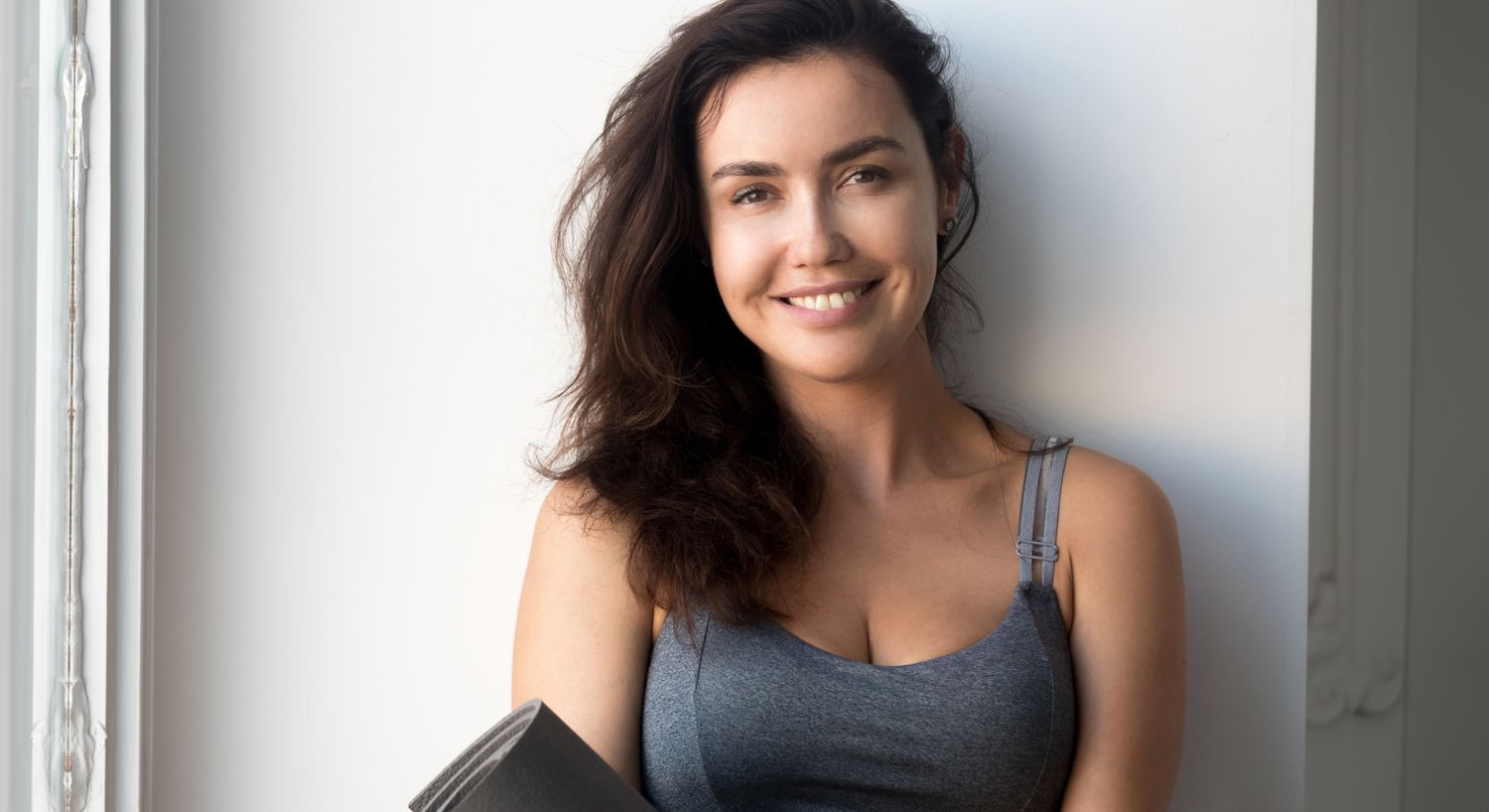 Smiling woman holding a yoga mat indoors.