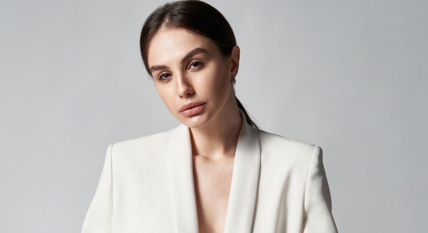 Woman in a white blazer, neutral background.